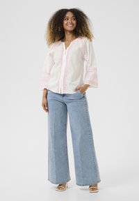 Blusa bianca con ricamo rosa, maniche a campana 3/4 e abbottonatura frontale. Abbinata a jeans a gamba larga blu chiaro e décolleté bianche aperte.