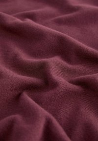 Tissu tricoté bordeaux avec une texture douce, présentant de légères rides et une finition lisse, indiquant un matériau de haute qualité.