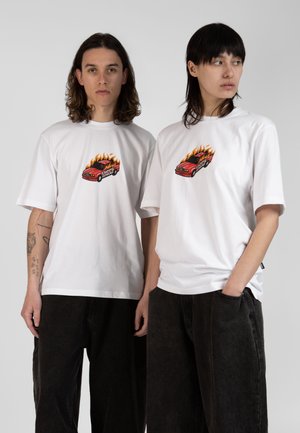 White graphic t-shirts feature a red car design with flames. Models wear loose black pants. The shirts have short sleeves and a relaxed fit.