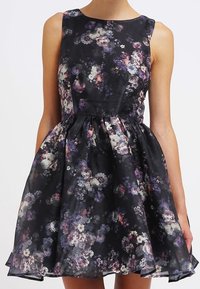 Blommig klänning med åtsittande liv och utsvängd kjol. Svart tyg med lila, vita och rosa blommor. Ärmlös design med rund halsringning.