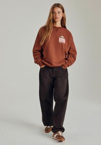 Brun sweatshirt med grafisk print på brystet, parret med mørke, løstsiddende bukser og sneakers med dyreprint. Glat stofstruktur.