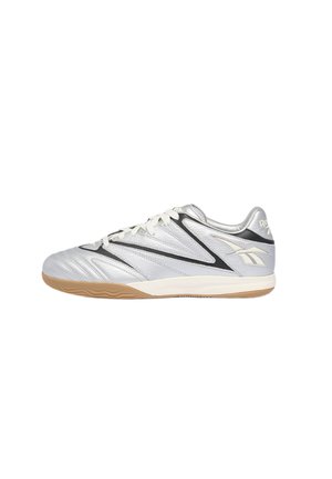 Silver and black low-top Reebok indoor soccer shoe with white laces and a gum rubber sole, side view on a white background.