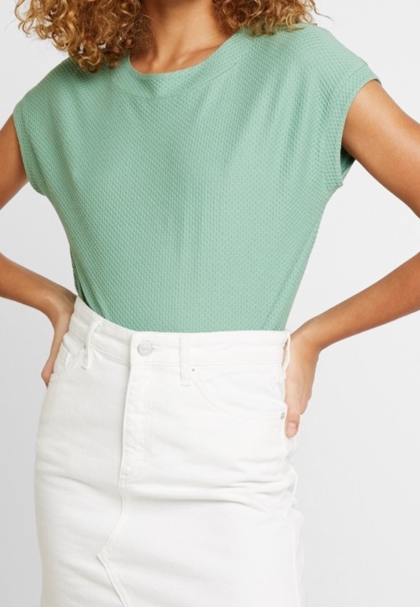 Světlý zelený strukturovaný top s krátkým rukávem v kombinaci s bílou džínovou sukní s vysokým pasem, která má design se záhybem a předním zapínáním na knoflík.