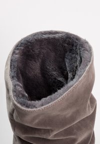 Botte en daim gris avec une doublure intérieure en fourrure épaisse et douce de couleur gris foncé, vue depuis l'ouverture supérieure sur un fond uni.