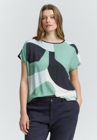 Korte mouwen blouse in lichtgroen, marineblauw en crème geometrische patronen; zachte stof met een relaxed fit en een ronde halslijn.