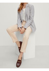 Blazer a rayas en azul claro y blanco, blusa crema, pantalones beige y mocasines marrón oscuro con acentos de hardware dorado. Texturas suaves.