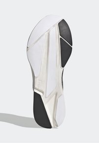 Suela de zapatilla en blanco y negro con una superficie texturada, surcos geométricos y un logotipo; cuenta con un borde de goma y una entresuela blanca lisa.