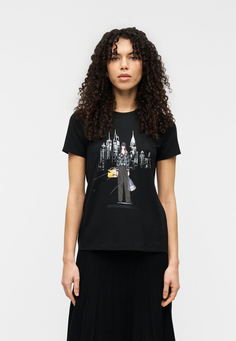 Μαύρο κοντομάνικο μπλουζάκι με γραφική απεικόνιση μιας μορφής σε φόντο ορίζοντα, συμπληρωμένο με λεπτομέρεια ενός κίτρινου ταξί.