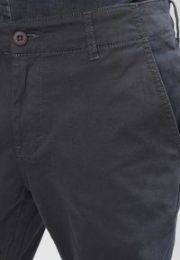 Pantaloni din bumbac gri închis, cu o textură netedă, detalii cusute și un închizător cu un singur buton la talie.