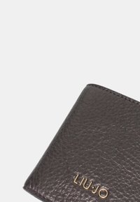Portafoglio in pelle nera texturizzata con logo dorato "LIU JO". Presenta un design semplice, una forma compatta e cuciture a contrasto lungo i bordi.