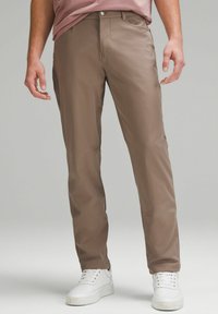 Ruskeat, kapea-muotoiset housut, joissa on sileä pinta ja etutaskut; yhdistetty valkoisiin lenkkareihin. Varustettu napin läppä ja vyölenkit.