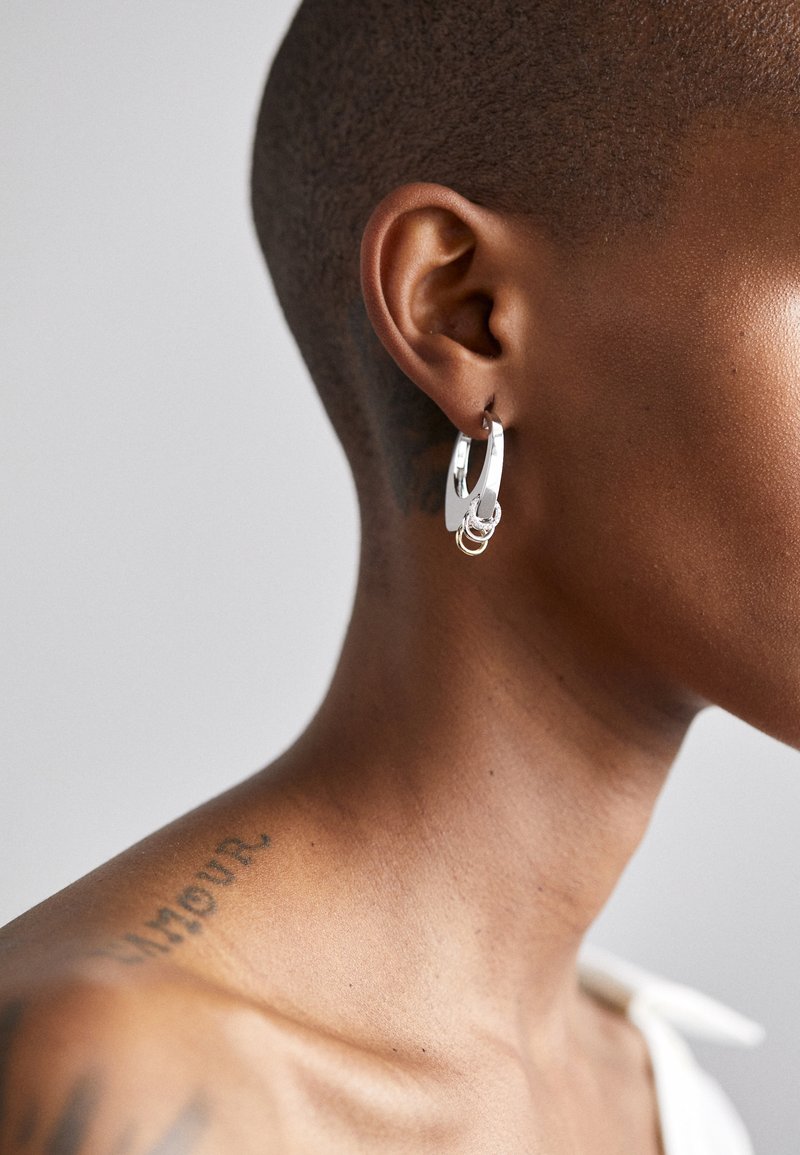 Ασημένια σκουλαρίκια κρίκοι με στρωματοποιημένο σχέδιο, που διαθέτουν μία μικρή χρυσή λεπτομέρεια. Λείος μεταλλικός φινίρισμα, τονίζοντας μια κομψή αισθητική.