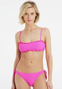 Karštai rožinė bikini maudymosi kostiumėlis, turintis tekstūruotą audinį, raukšlėtą apdailą ant bandeau viršaus ir reguliuojamas raištelių šonus apatiniuose.