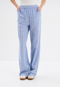 Blauwe gestreepte wijde broek met een elastische tailleband, met lichte en donkerblauwe verticale lijnen en zakken aan de zijkanten.