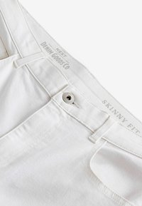 Weiße, eng anliegende Jeans aus Denim mit einem Metallknopfverschluss und einem gesteppten Taillenbund. Markenlabel auf dem Taillenbund sichtbar.
