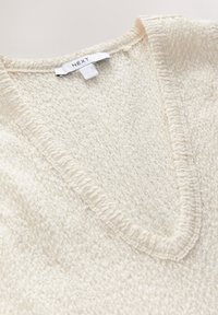 Maglione color crema con design a V, tessuto testurizzato e bordo cucito lungo il collo. Etichetta con la scritta "NEXT."