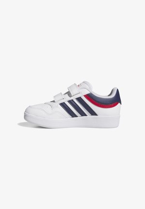 Zapatilla blanca con rayas azul marino, detalle rojo cerca del talón y dos bandas de velcro, mostrada de perfil sobre un fondo blanco.