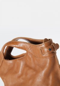 Braune Lederhandtasche mit glatter Struktur, offenem Oberteil und Seitengriffen. Enthält ein Schnallendetail am Tragegurt.