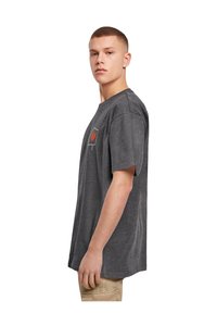 Mørkegrå t-shirt med korte ærmer og afslappet pasform, prydet med et rødt og hvidt emblem på brystet. Materiale af bomuldsblanding.