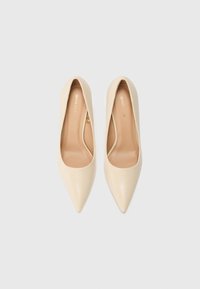 Scarpe con tacco alto beige dal design a punta. Texture liscia, silhouette minimalista, con un collo del piede basso e una suola interna con logo discreto.