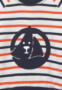 Gestreifter Sweatshirt mit weißen und marineblauen Streifen sowie orangen Akzenten. Zentrales marineblaues Patch zeigt ein Segelboot und ein Bärenkopf in Weiß.