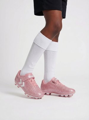 Nogi w czarnych szortach, białych podkolanówkach i błyszczących różowych korkach piłkarskich na jednolitym tle.