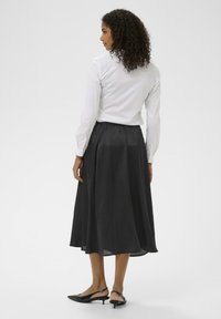 Fekete midi szoknya laza szabással, ráncolt derékkal és fényes felülettel, egy szűk fehér inggel és fekete slingback cipőkkel párosítva.