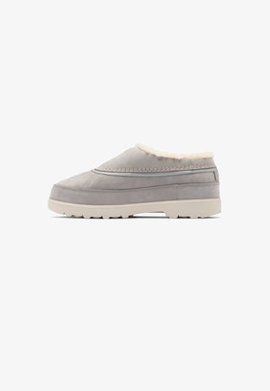 Lysegrå slip-on sko med tyk beige sål og blød hvid pelsforing, vist i sidevisning på hvid baggrund.