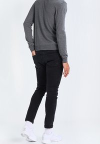 Grau gestrickter Pullover, schwarze Slim-Fit-Jeans und weiße Sportschuhe. Stricktextur des Pullovers und sichtbare Knöchelsocken.