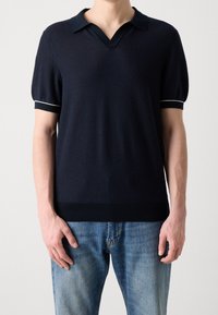 Polo bleu marine à manches courtes avec col en V, ourlet côtelé et bordure blanche contrastante sur les manches. Fabriqué dans un tissu texturé.