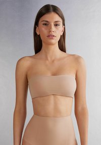 Beige strapless bandeau-top met een gladde textuur en naadloos ontwerp, gecombineerd met een hoog getailleerde onderkant in bijpassende kleur. Geen patronen of accenten zichtbaar.