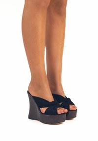 Sandali wedge neri con cinturini in tessuto annodati, piattaforma texturizzata marrone scuro, design open toe e una leggera lucentezza sul materiale.