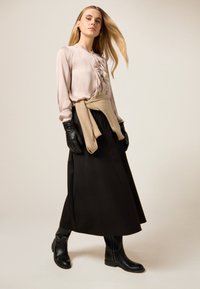 Lång svart kjol, ljusrosa blus med volanger, beige tröja knuten i midjan, svarta handskar och ankelboots med kontrasterande sömmar.