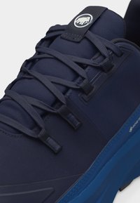 Μπλε ναυτικό αθλητικό παπούτσι με χοντρή μπλε σόλα, διακοσμημένο με ετικέτα Gore-Tex, στρογγυλεμένη μύτη και μαύρα κορδόνια περασμένα μέσα από υφασμάτινες τρύπες.