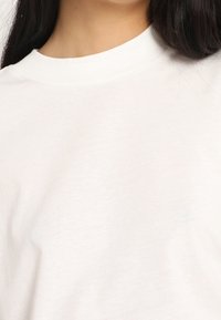 Camiseta blanca de algodón con cuello redondo, mangas cortas y textura suave, que muestra la sutil suavidad de la tela y un color uniforme.