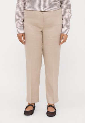 Osoba ubrana w beżowe spodnie z prostymi nogawkami, brązowo-białą koszulę w paski zapinaną na guziki oraz czarne buty Mary Jane z klamrami.