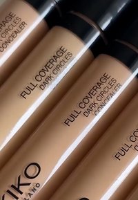 Concealer-Tuben in einem nude beigen Farbton mit schwarzen Kappen. Die Etiketten tragen die Aufschrift "FULL COVERAGE DARK CIRCLES" und zeigen ein mattes Finish.