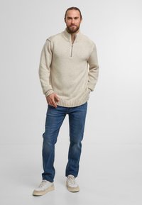 Cremefarvet strikket sweater med halvlukket krave og ribbede manchetter, parret med blå denimjeans og lyse sneakers.