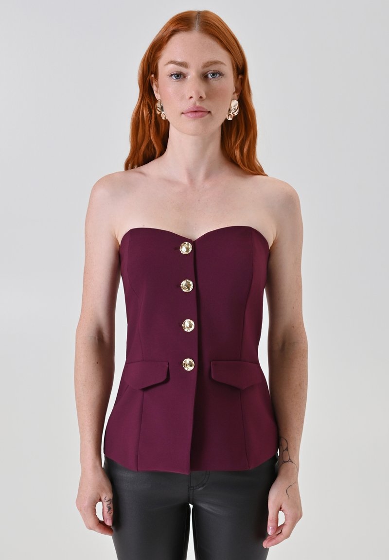 Top senza spalline di colore burgundy con design aderente, quattro bottoni dorati e due tasche frontali. Texture liscia, silhouette sartoriale.