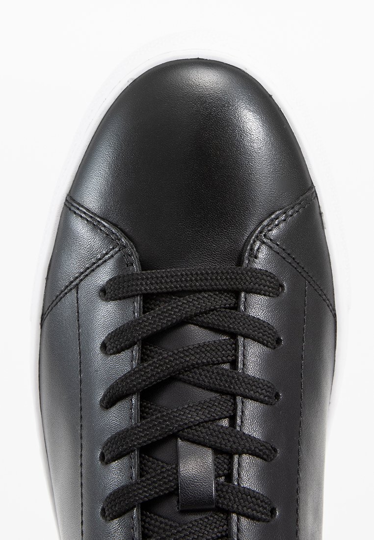 Sneaker in pelle nera con punta arrotondata, parte superiore texturizzata e lacci neri. Presenta una suola in gomma bianca e dettagli di cucitura discreti.