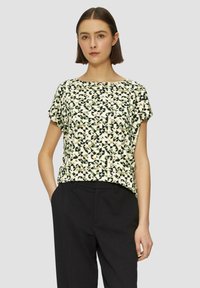 Korte mouw top in crèmekleurige stof met een geometrisch patroon in zwart, groen en bruin. Eenvoudige ronde hals en een relaxte pasvorm. Gepaard met zwarte broek.