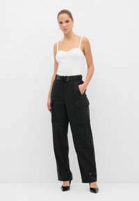 Zwarte cargobroek met zakken, gecombineerd met een witte aansluitende tanktop en een zwarte riem. De broek heeft knoopaccenten aan de zoom.