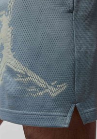 Blå sports SHorts med et tekstureret, åndbart stof, der har et let grafisk design på siden og en lille ventileret kant.