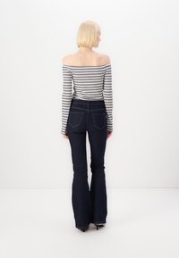 Randig off-the-shoulder topp med lång ärm, kombinerad med utsvängda mörka jeans i denim med bakfickor och kontrasterande sömmar.