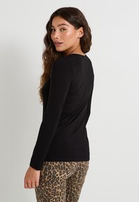 Haut noir à manches longues en matériau lisse, design ajusté avec col rond, associé à des leggings imprimé léopard avec un motif texturé.