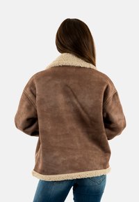 Chaqueta de ante sintético marrón con un cuello y dobladillo de piel de oveja beige, con un corte relajado y mangas largas, mostrada desde la parte de atrás.