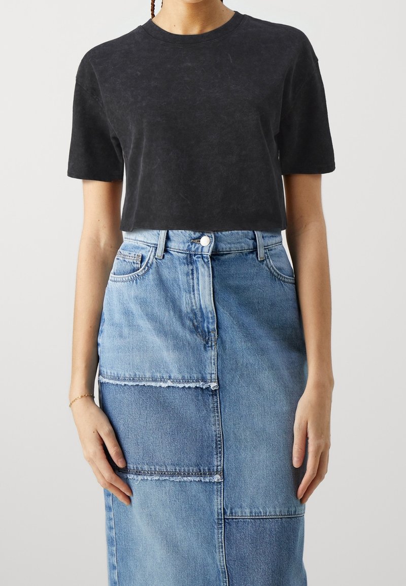 T-shirt noir court avec des manches courtes et un col rond, associé à une jupe en denim bleu avec des détails en patchwork et des bords effilochés.