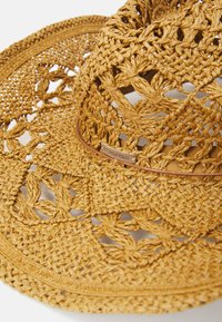 Cappello di paglia intrecciato di color beige chiaro, con una larga tesa, motivi intricati e una fascia decorativa marrone con il testo "ORA È STUFO."