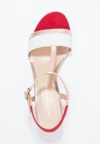 Sandale ouverte rouge en daim avec des straps blancs et rose doré, dotée d'une boucle brillante en rose doré. Doublure intérieure lisse et silhouette élégante.