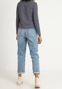 Randig marinblå långärmad topp med rund halsringning, tillsammans med ljusblå jeans med uppvikta ben. Ljusbeiga ankelstövlar fulländar outfiten.